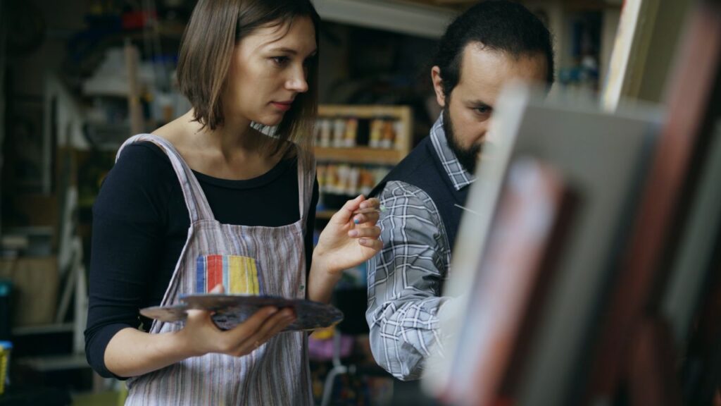 Two artists engaged in painting, focused on their creative process in a studio.