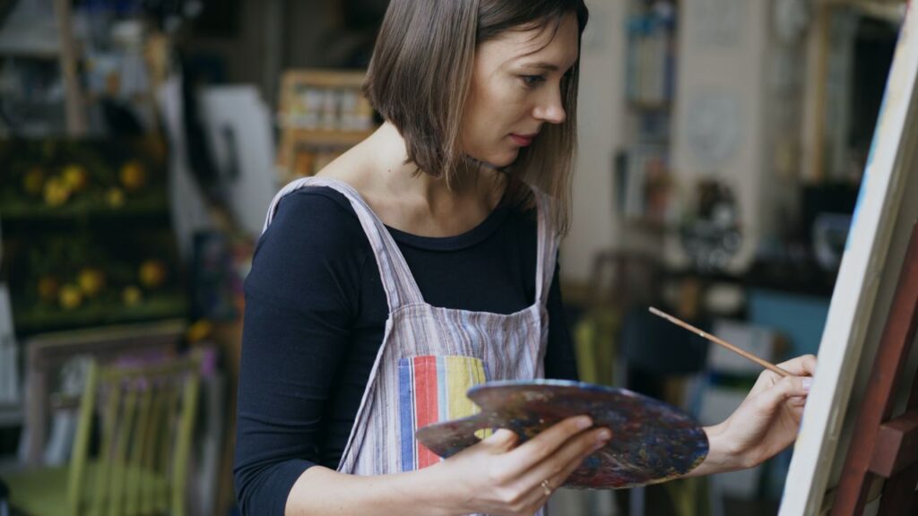 Focused female artist creating artwork on canvas indoors.