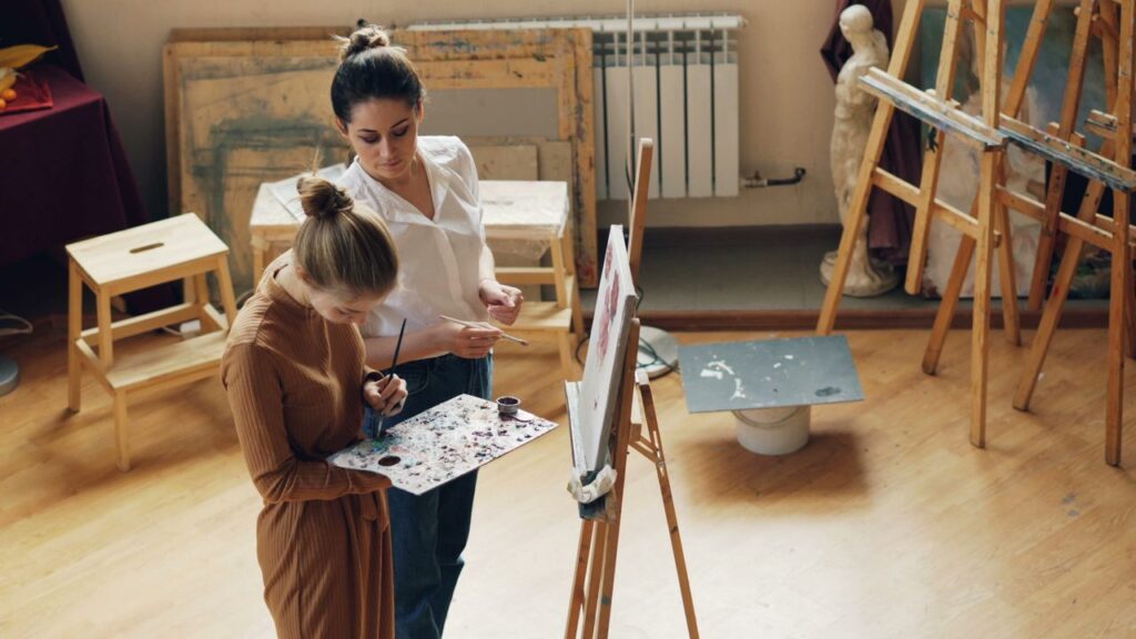 Two women artists creating paintings together in a cozy indoor art studio.