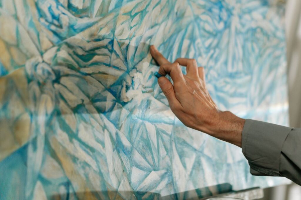 Close-up of a hand applying pastel to a canvas with blue abstract patterns, showcasing creativity.
